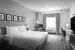 A hotel bedroom with a king-sized bed against a pink wall, an armchair by a window, and a work desk.