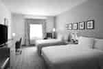Guest room with two beds, a desk with a TV and chair, an armchair, and a window with patterned curtains.