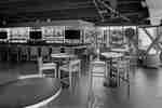 Hotel bar with a stocked counter, barstools, tables, and lounge chairs by large windows