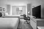 Guest room with two beds, a work desk, TV, and a window seat with city buildings outside