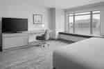 Guest room with a bed, TV, work desk, chair, and large window with buildings outside