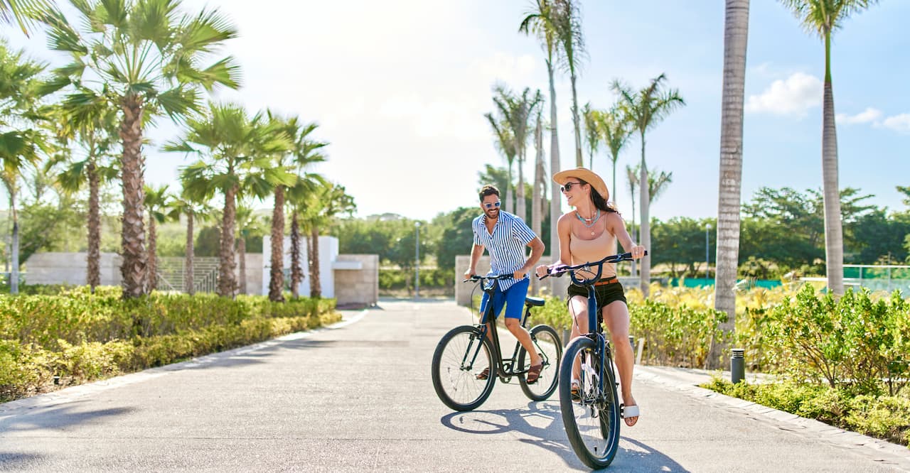Man and woman pedal bikes next to palm trees