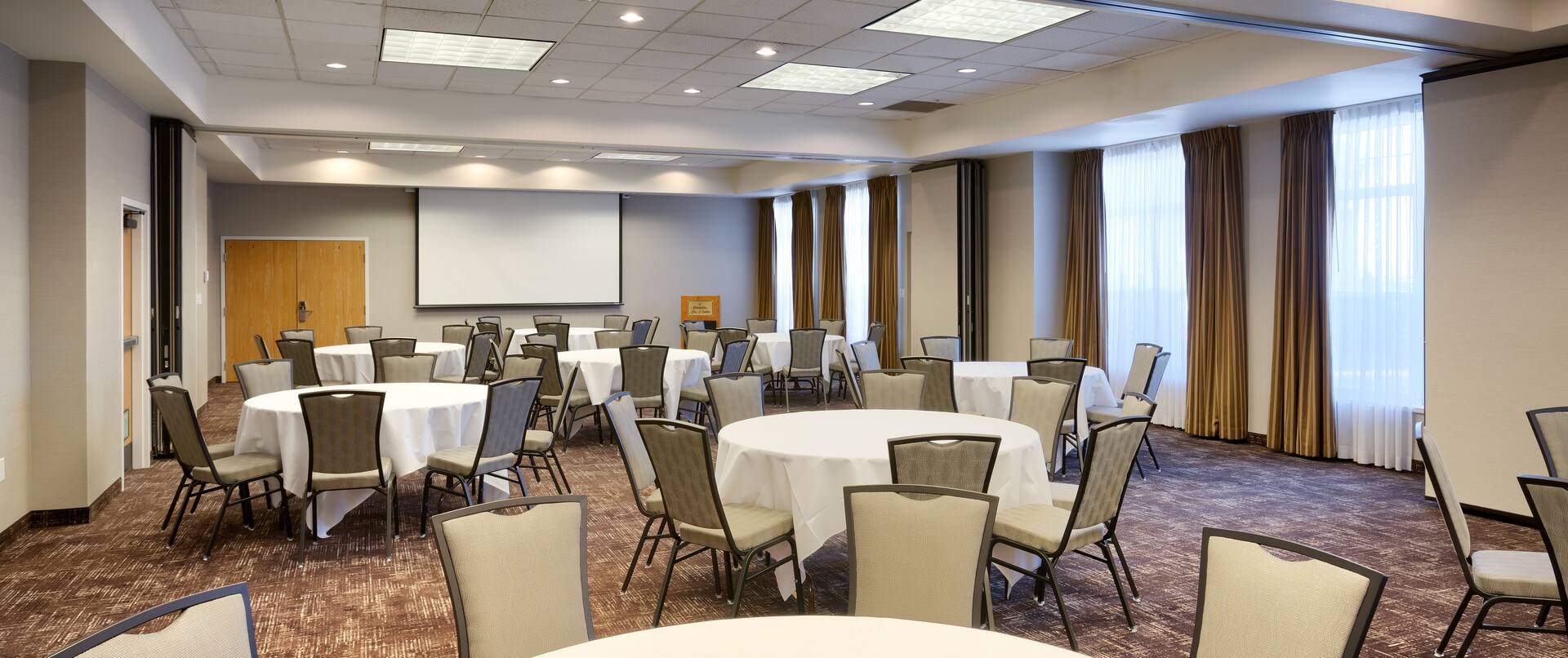 Meeting Room With Presentation Screen, Podium, Chairs and White Linens on Banquet Tables 