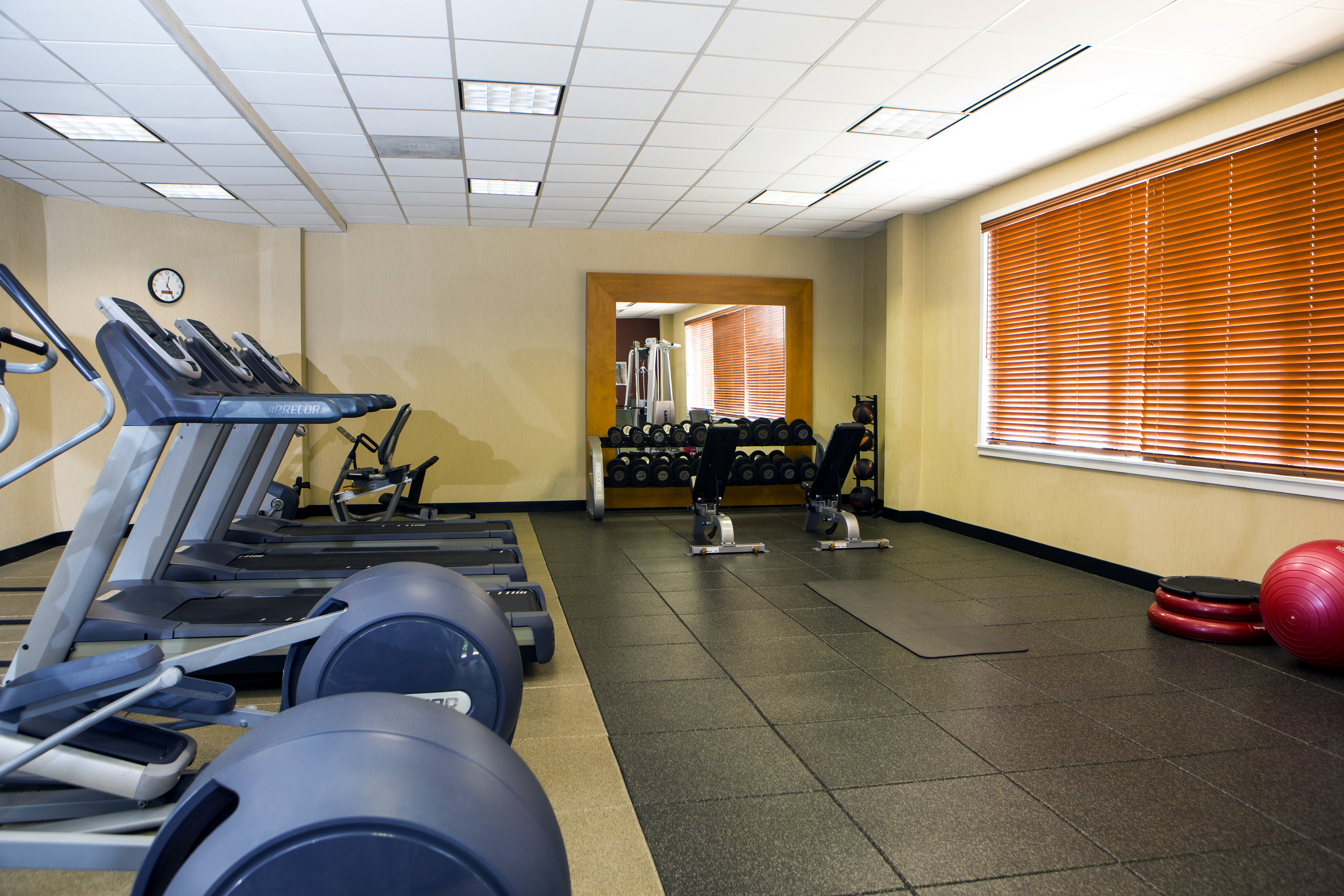 Fitness Room With Cardio Equipment, Wall Clock, Free Weights, Weight Benches, Aerobic Stepper, and Red Exercise Ball