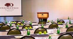 Classroom Setup in Meeting Room With Bottled Water, Green Apples, and Note Pads on Tables, Chairs, Presentation Screen, and Podium