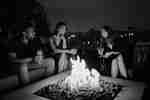 Three people with drinks sitting around a firepit