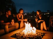 Three people with drinks sitting around a firepit