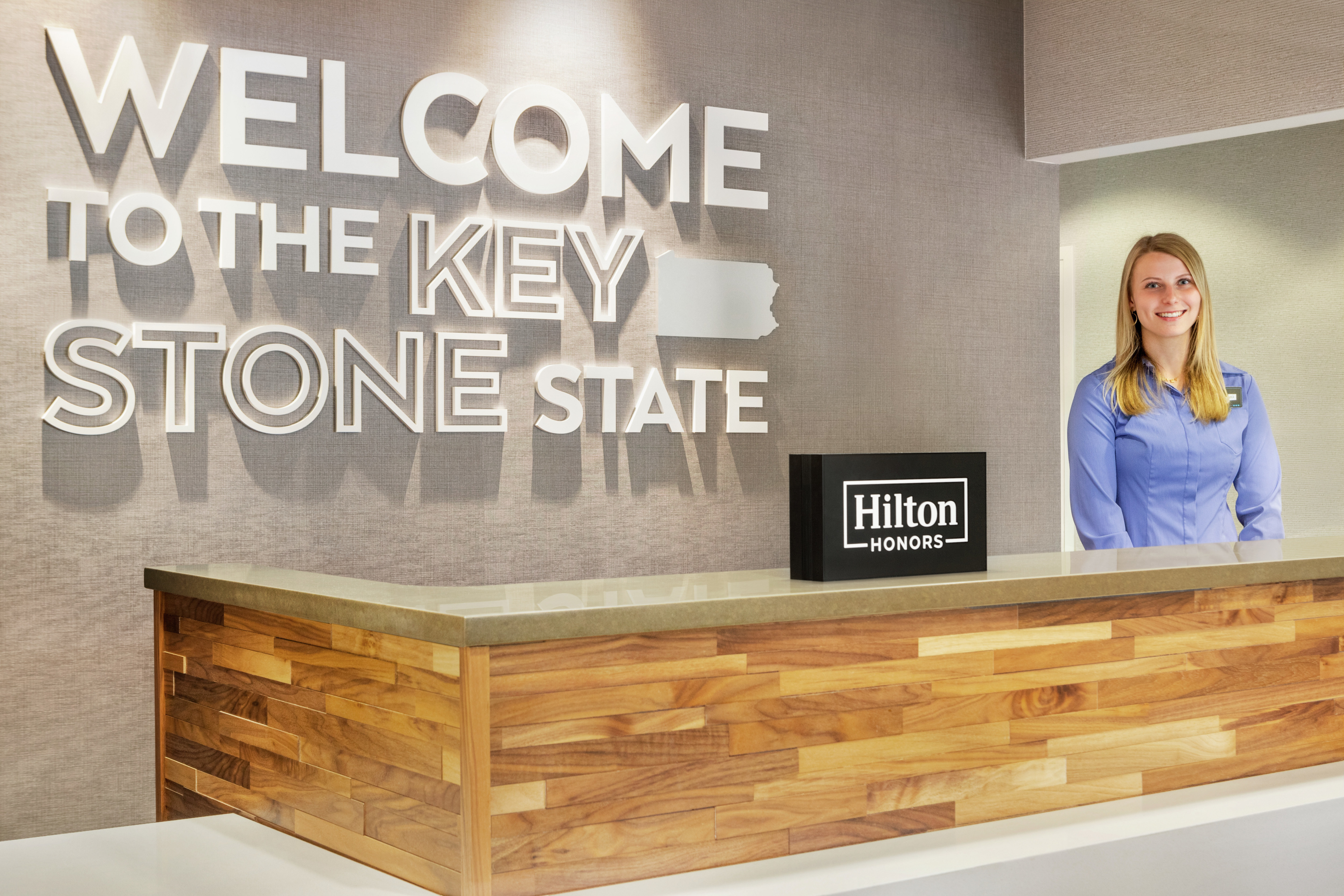 Bright and inviting hotel front desk, featuring Key Stone State wall art and welcoming hotel staff member