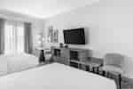Guest room with two beds, a work desk, a wall-mounted TV, and a soft chair.