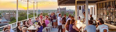 A vibrant rooftop bar scene featuring patrons seated at tables, enjoying drinks and socializing
