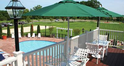 Deck with Umbrella-Covered Tables Overlooking Pool and Field