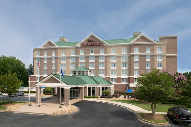 Aerial View of Hotel Exterior, Signage, Flagpoles, Landscaping, Porte Cochère, and Guest Cars on Parking Lot