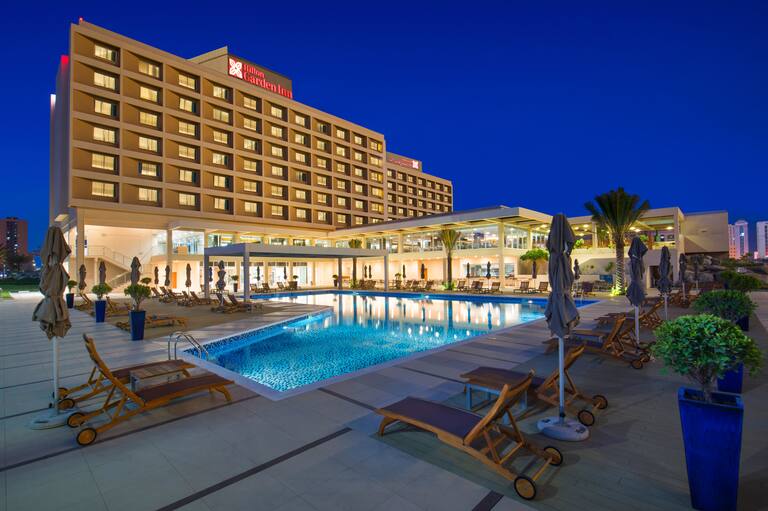 Verlichte buitenkant hotel met borden en zwembad bij nacht
