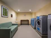 Coin Operated Washing and Drying Machines, Green Sofa and Folding Table in Laundry Facility