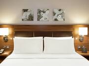 Wall Art Above Neatly Made King Bed Between Two Illuminated Lamps and Bedside Tables 
