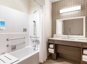 Spacious accessible bathroom featuring large vanity, mirror, and tub with convenient shower seat.
