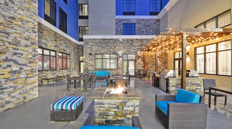 Outdoor Patio Seating By Fire Pit and Grill Area Under Pavilion With Illuminated String Lights at Dusk 