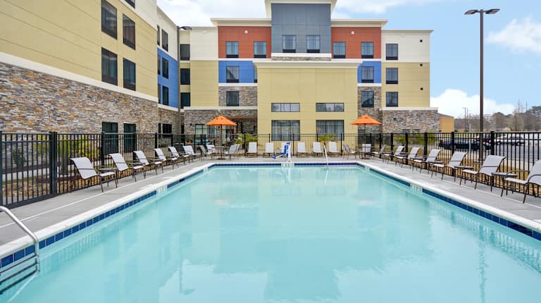 Daytime View of Hotel Exterior and Outdoor Pool Surrounded by Chairs