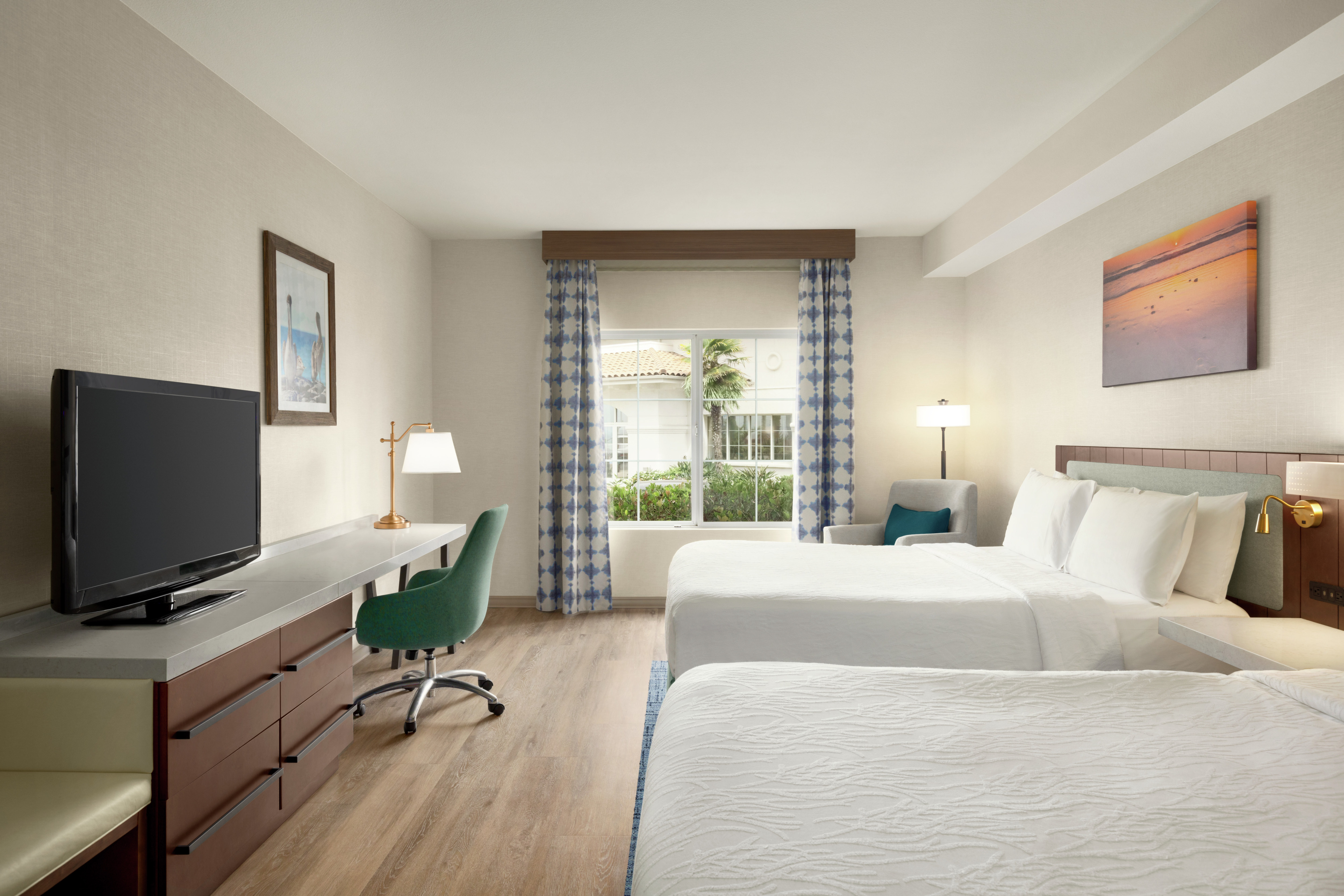 Spacious guest room featuring two comfortable queen beds, TV, work desk, and outside view.