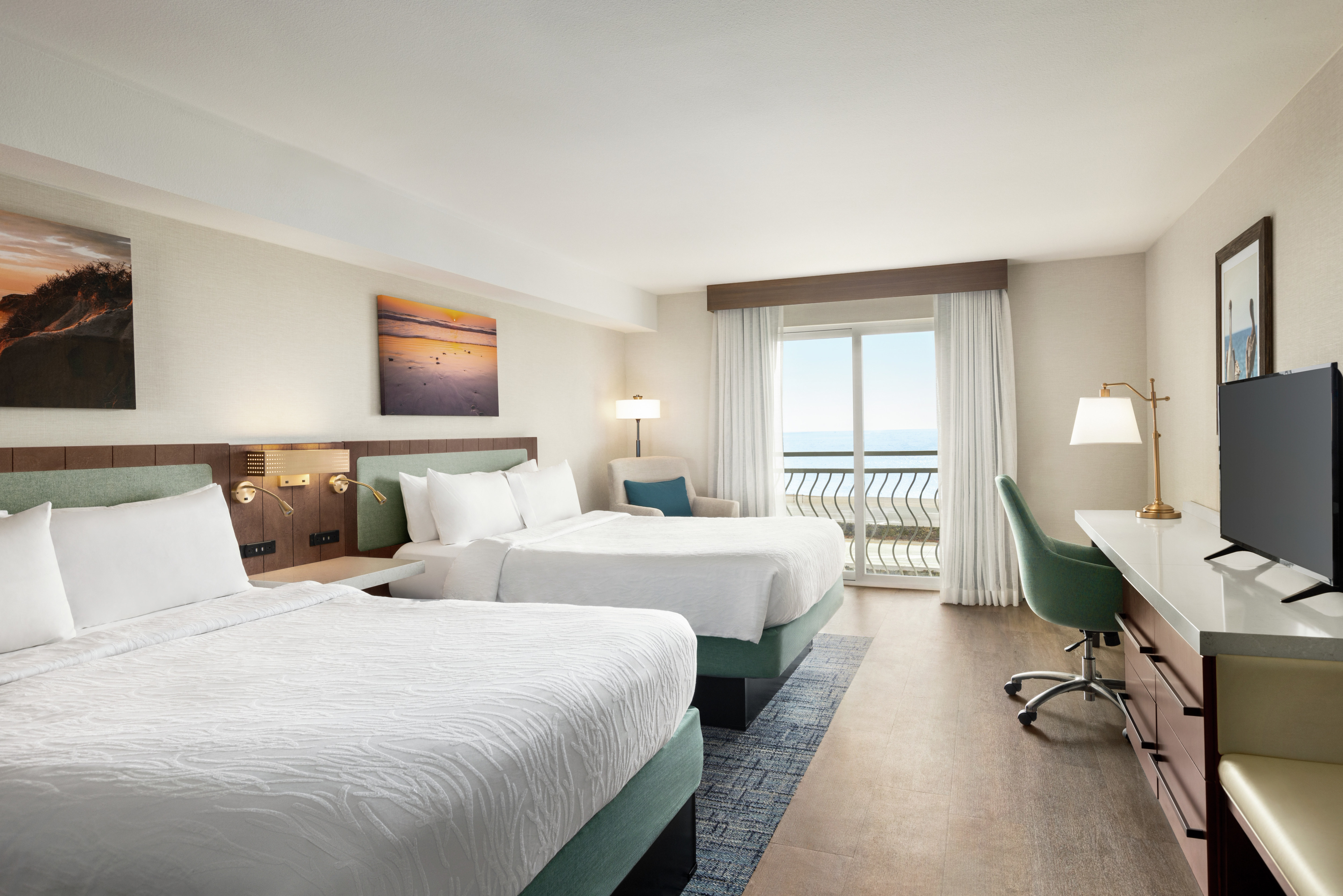 Spacious guest room featuring two comfortable queen beds, TV, work desk, and ocean view.