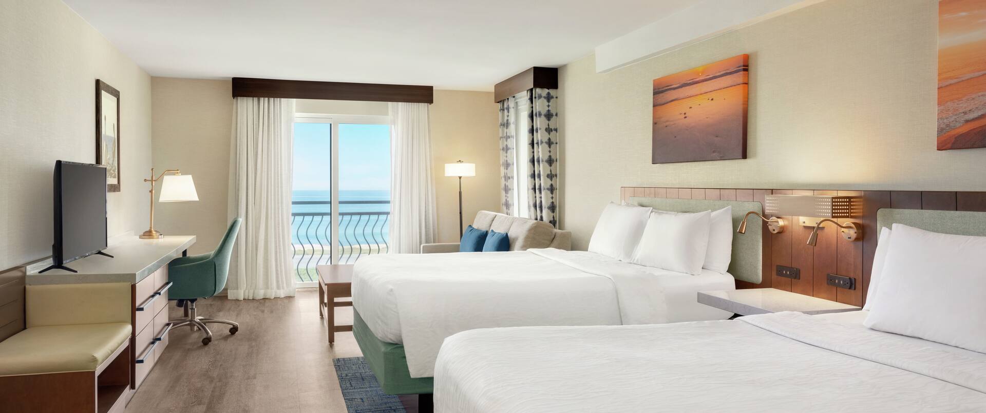 Spacious deluxe guest room featuring two comfortable queen beds, TV, work desk, and stunning ocean view.