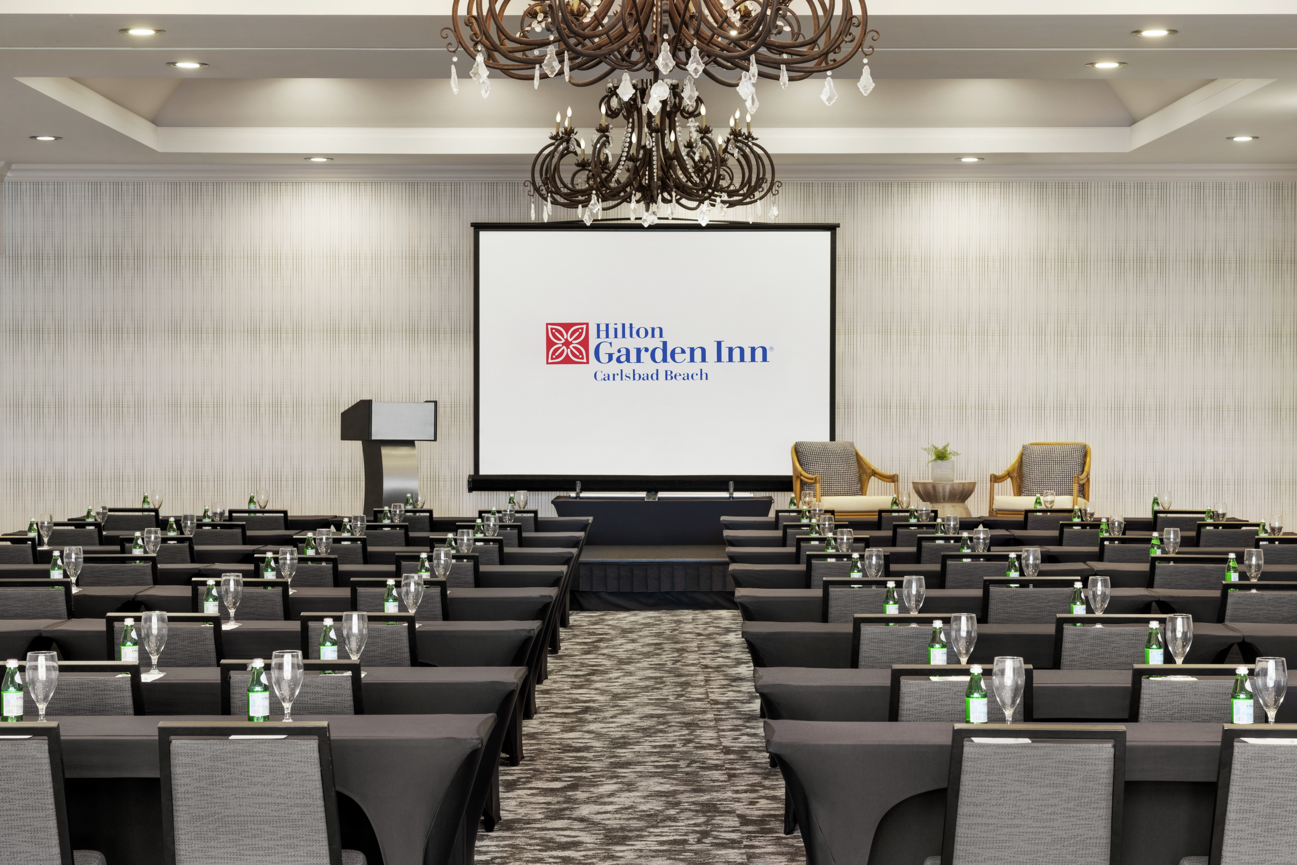 Spacious on-site ballroom featuring classroom style seating with stage, podium, and projector screen at front of room.