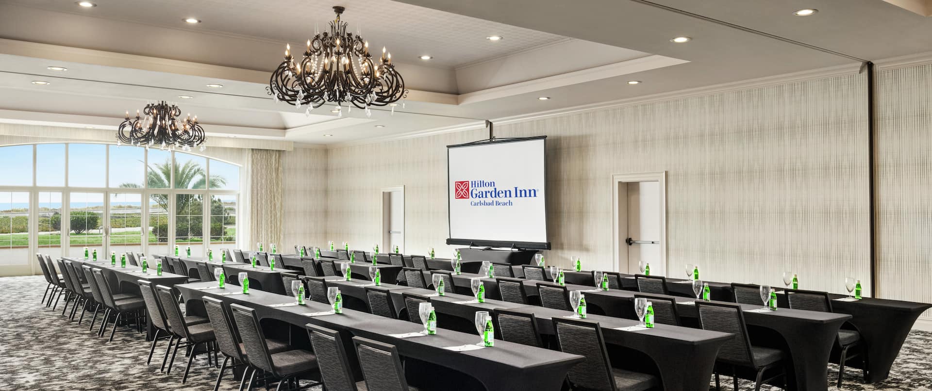 Spacious on-site ballroom featuring ample classroom style seating, large window, and projector screen at front of room.