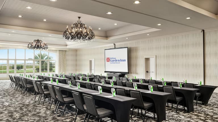 Spacious on-site ballroom featuring ample classroom style seating, large window, and projector screen at front of room.