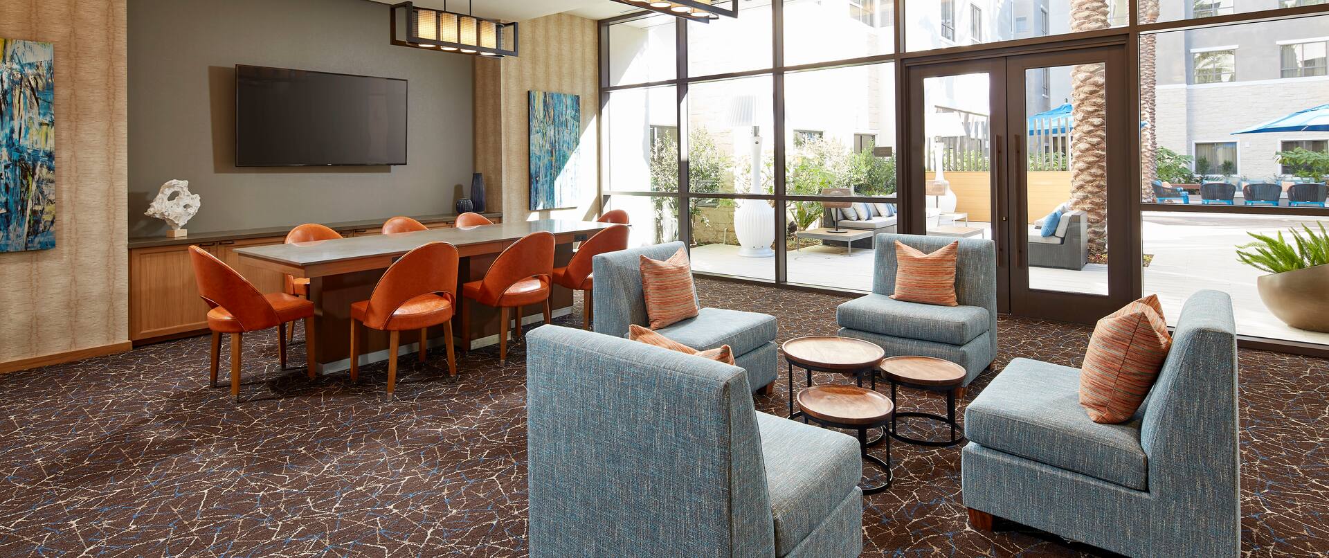 Interior Common Seating Area with HDTV, Four Cushioned Chairs, a Table with Seating for Eight, and a View of the Patio through the Floor-to-Ceiling Windows and Doors