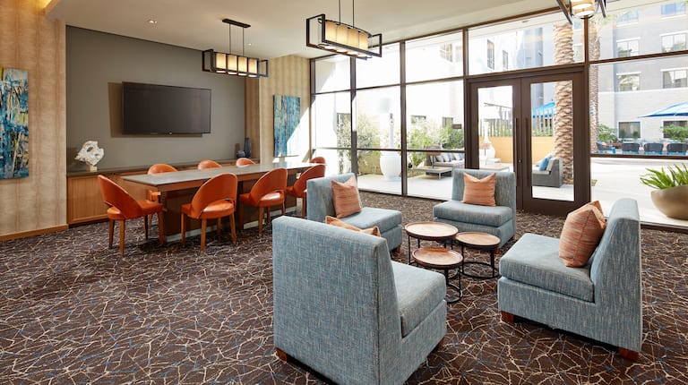 Interior Common Seating Area with HDTV, Four Cushioned Chairs, a Table with Seating for Eight, and a View of the Patio through the Floor-to-Ceiling Windows and Doors