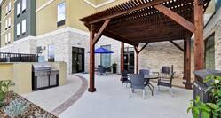 Daytime View of Hotel Exterior, Landscaping, Grill, Table With Blue Umbrella, and Seating Under Pavilion on Patio