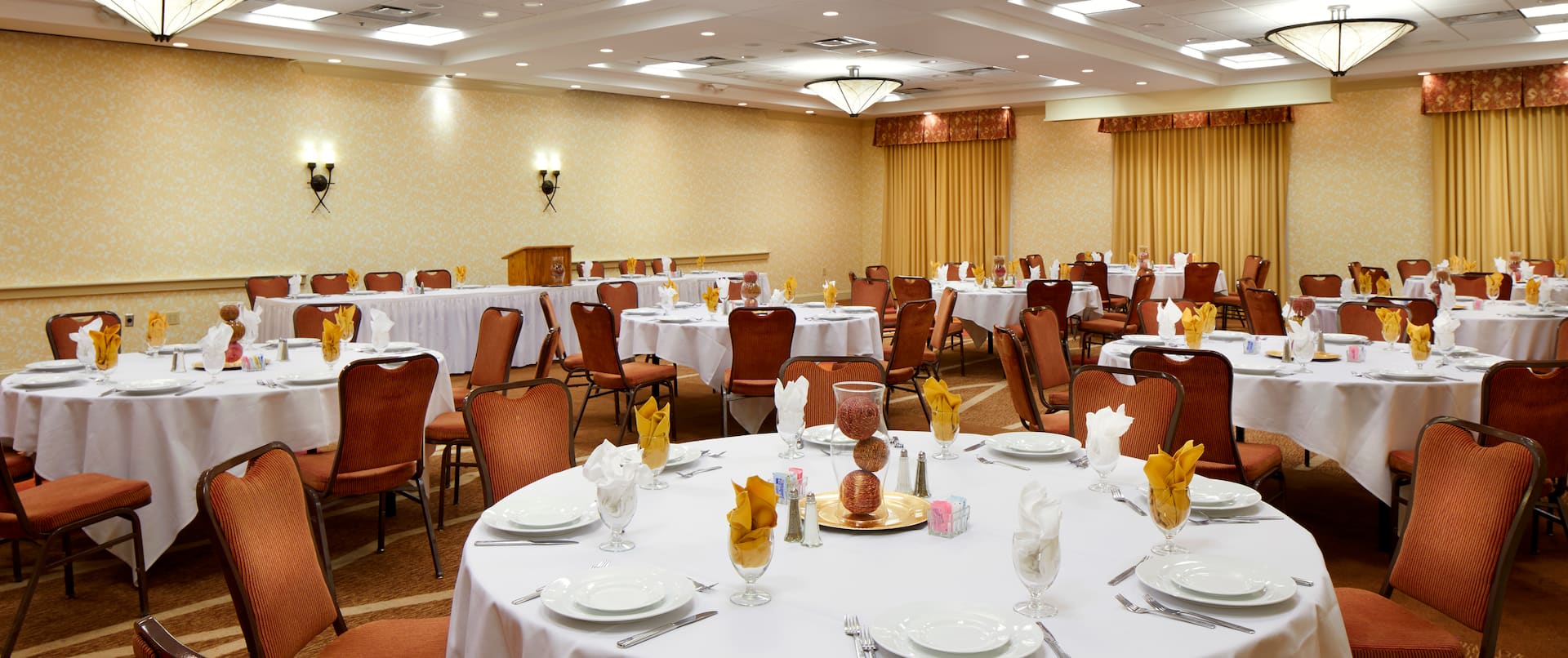 Chairs, Place Settings, Decorative Centerpieces, and White Linens on Round Tables in Ballroom Set Up for Banquet