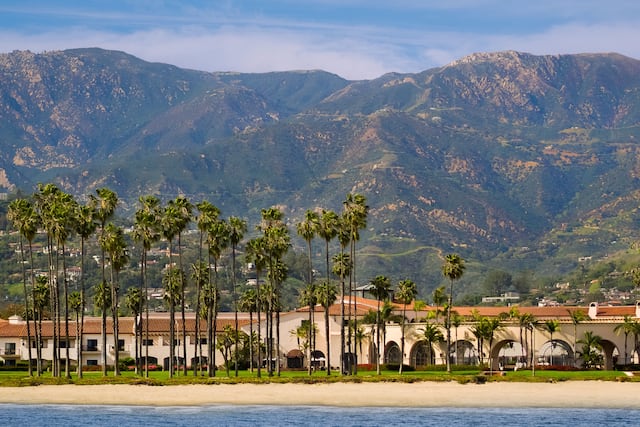 Dramatic Beach Front View of Hotel Lined with Palm Trees and Mountains Behind