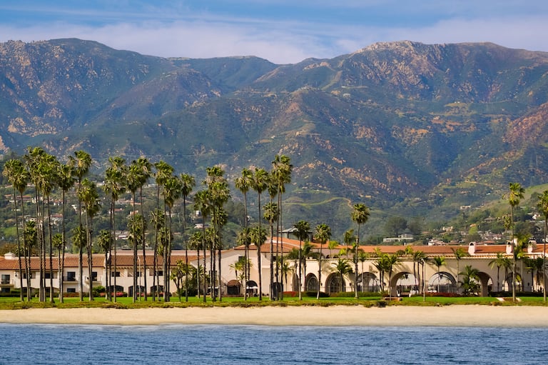Dramatic Beach Front View of Hotel Lined with Palm Trees and Mountains Behind