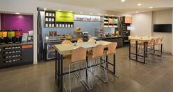 Breakfast serving area with coffee, juice, cereals, pastries, waffle station, dining amenities, and high tables with chairs