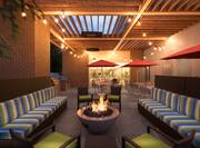 Outdoor patio area lit up with sofas and lounge chairs surrounding fire pit, and tables with umbrella covers