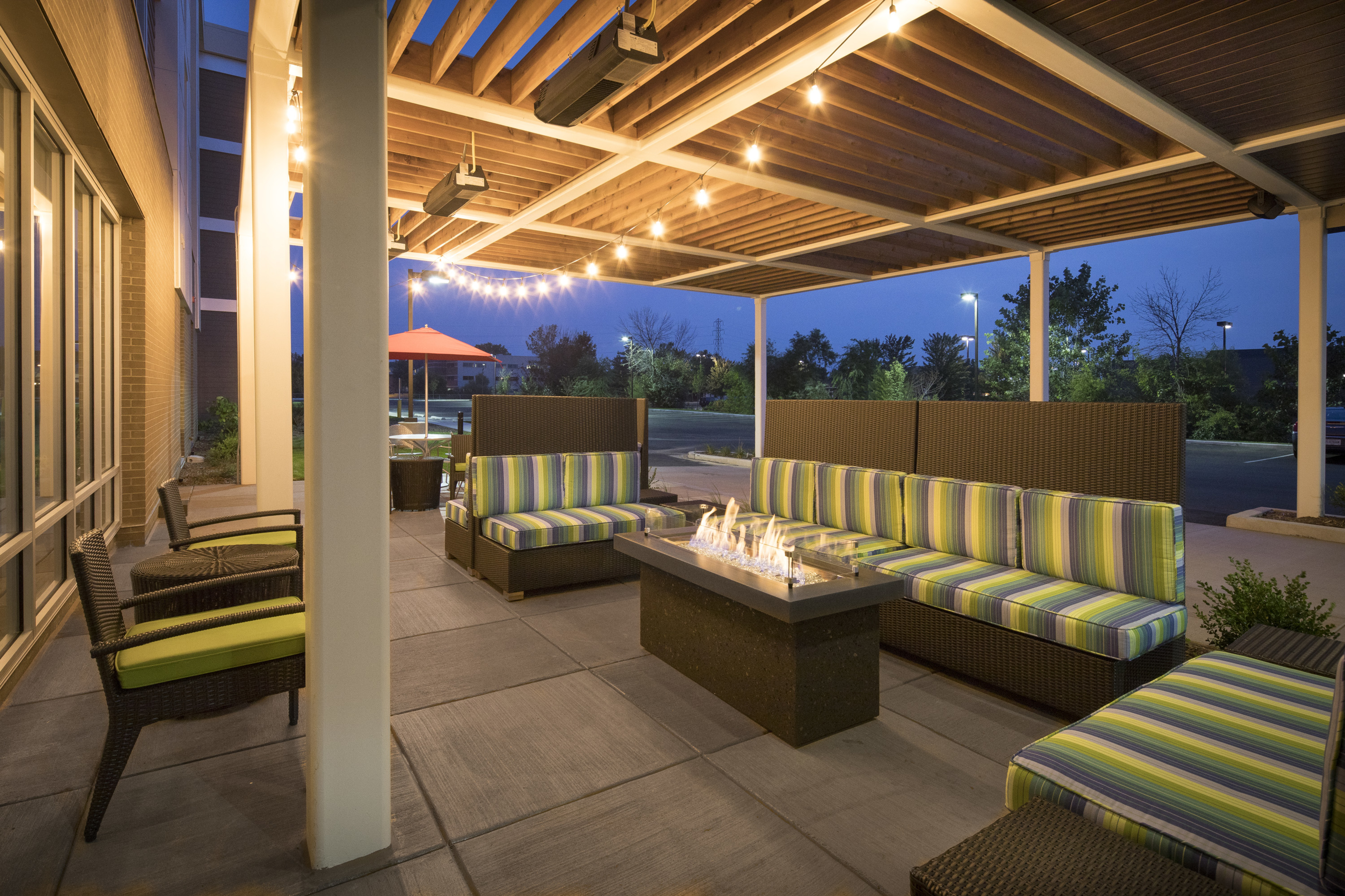 Outdoor patio area lit up with sofas and lounge chairs surrounding fire pit