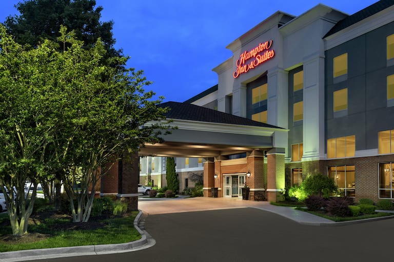 Welcoming Hampton Inn hotel exterior featuring porte cochere, glowing guestrooms, and lush landscaping.