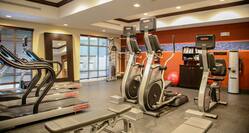 Fitness Center With Cardio Equipment, Large Mirror Between Two Windows, Weight Machine, Red Stability Ball, Towel Station, and Water Cooler