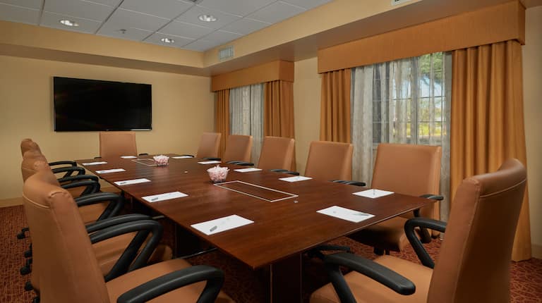 Conference Room Boardroom Set Up with Office Chairs, Large Table, Notepads and Wall Mounted HDTV