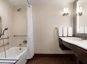 Spacious accessible bathroom featuring tub with shower seat, grab bars, large vanity, and mirror.