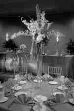 Židle, stolky pro hlavu a hosty s jídelním lístkem, ubrousky s ventilátorem a květiny na zlatých povlečeních v taneční sále připravené na svatební recepci