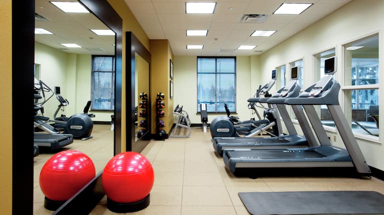 Fitness Center With Red Exercise Ball, Large Mirrors, Weight Balls, Free Weights, Weight Bench, Window, and Cardio Equipment