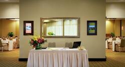 Two Chairs, Flowers, and Laptop on Registration Table With White Linens, and View into Meeting Space With Classroom Set Up