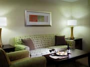 Table With Room Service, Armchair, Illuminated Lamps, and Wall Art Above Sofa in Living Room Suite