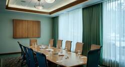 Seating for 12, Water Pitchers, Drinking Glasses, and Notepads at Connectivity Table in Boardroom With Media Cabinet, and Windows With Long Drapes