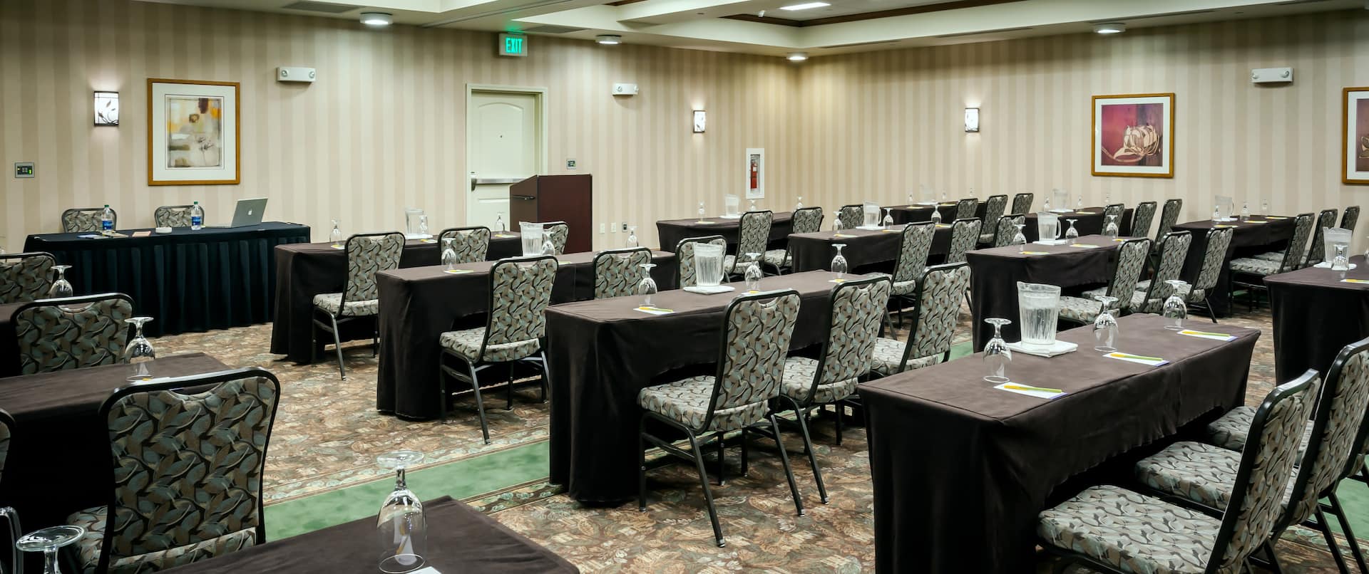 Classroom Setup in Meeting Room With Tables and Chairs Facing Speaker's Table With Laptop, Two Chairs, and Podium