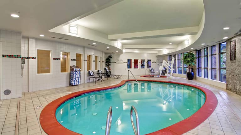 Indoor Swimming Pool and Whirlpool With Towel Station, Table, Chairs, Lounger, and Windows