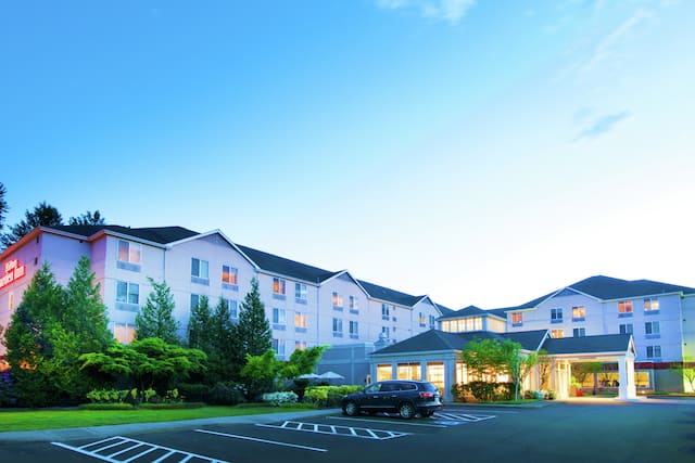  Illuminated Hotel Exterior With Signage, Landscaping, and Guest Cars on Parking Lot at Dusk