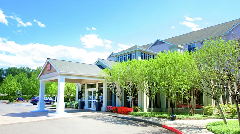 Daytime View of Hotel Exterior, Hotel Entrance, Landscaping, Porte Cochère, and Guest Cars on Parking Lot